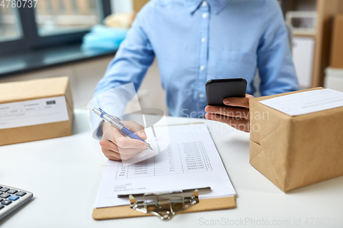 Image of woman with smartphone and clipboard at post office