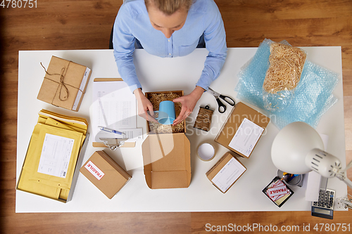 Image of woman packing mug to parcel box at post office