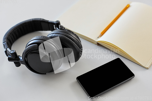 Image of headphones, smartphone and notebook with pencil