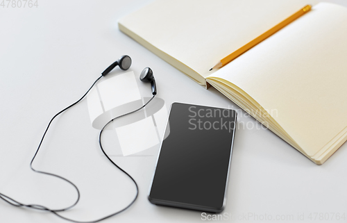 Image of earphones, smartphone and notebook with pencil