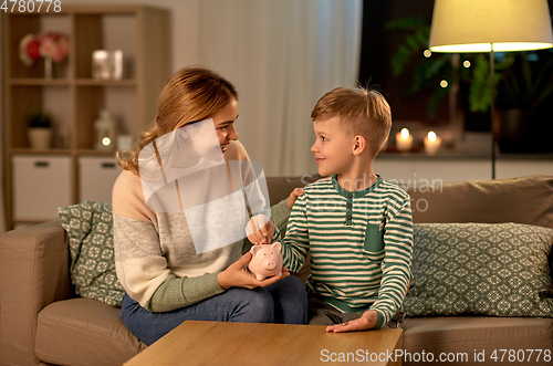 Image of mother and little son with piggy bank at home