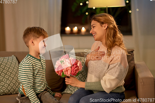 Image of smiling little son gives flowers to mother at home