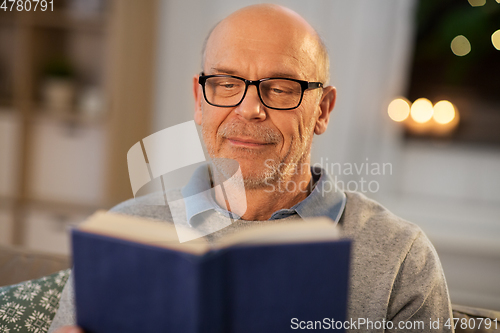 Image of happy bald senior man on sofa reading book at home