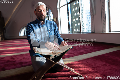 Image of muslim man praying Allah alone inside the mosque and reading islamic holly book