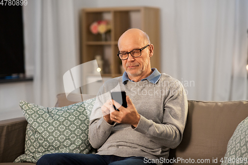 Image of senior man texting on smartphone at home