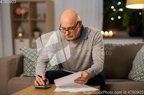 Image of old man with bills counting on calculator at home