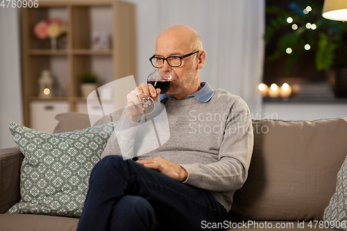 Image of senior man drinking red wine from glass at home