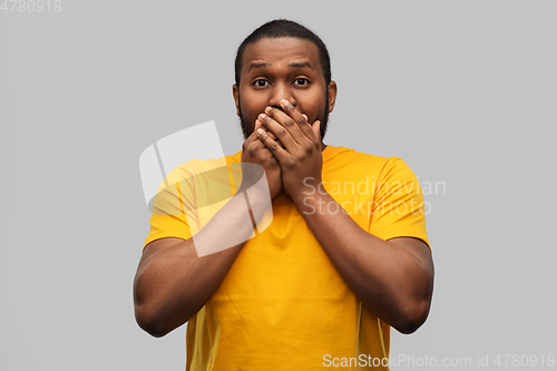 Image of scared african american man covering his mouth