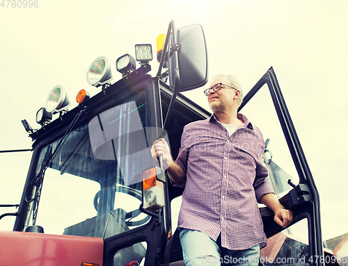 Image of old man or farmer getting out of tractor at farm