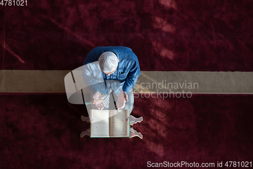 Image of muslim man praying Allah alone inside the mosque and reading islamic holly book