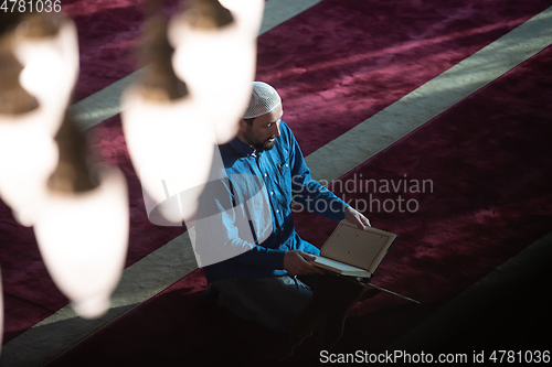 Image of muslim man praying Allah alone inside the mosque and reading islamic holly book