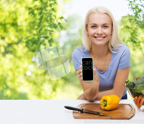 Image of smiling woman with smartphone cooking vegetables