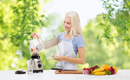 Image of smiling woman with blender making fruit smoothie