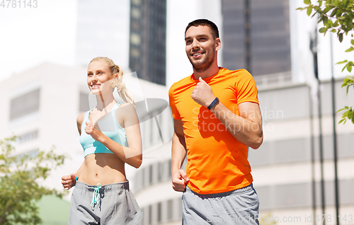 Image of happy couple with fitness trackers running at city