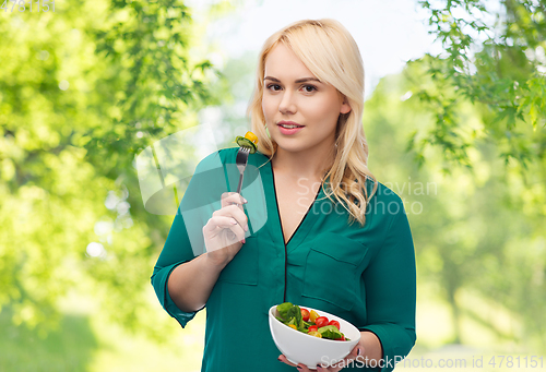 Image of smiling young woman eating vegetable salad