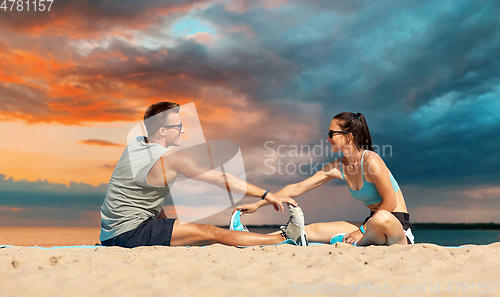 Image of smiling couple stretching legs on beach