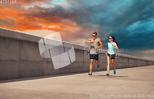 Image of couple in sports clothes running along pier