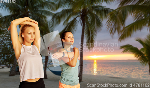 Image of women with fitness trackers stretching on beach