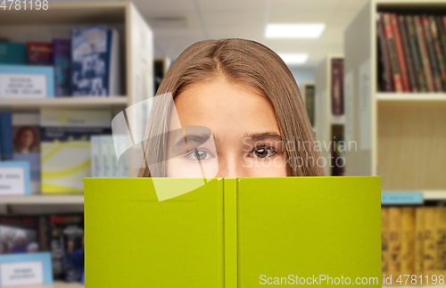 Image of teenage student girl hiding over book at library