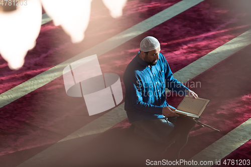 Image of muslim man praying Allah alone inside the mosque and reading islamic holly book