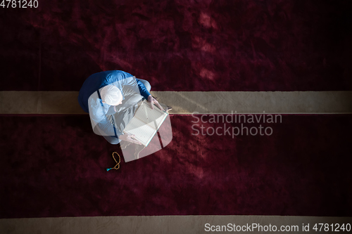 Image of muslim man praying Allah alone inside the mosque and reading islamic holly book