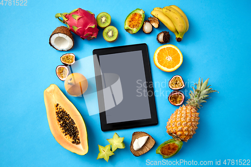 Image of fruits around tablet computer on blue background