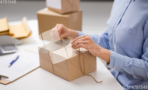 Image of woman packing parcel and tying rope at post office