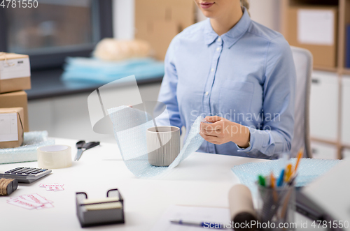 Image of woman packing mug to parcel box at post office