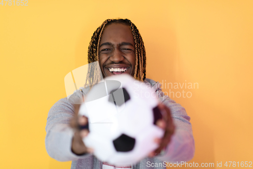 Image of afro man posing on a yellow background while holding a soccer ball