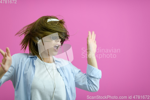 Image of brunette lady in black glasses dancing and listening music isolate on pink background