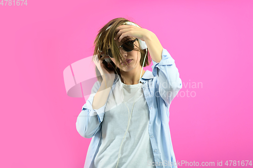 Image of brunette lady in black glasses dancing and listening music isolate on pink background