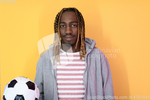 Image of afro man posing on a yellow background while holding a soccer ball
