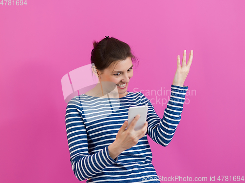 Image of a surprised-faced girl looks at her cell phone as she stands in front of a pink background