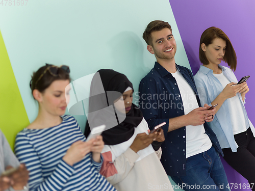 Image of diverse teenagers use mobile devices while posing for a studio photo in front of a pink background