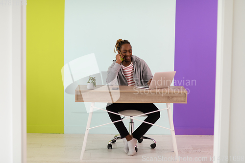 Image of afro young man sits in his home office during a pandemic and uses the phone