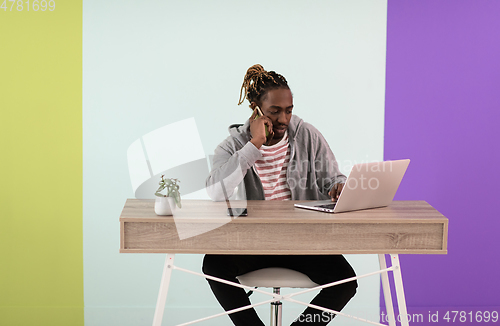 Image of afro young man sits in his home office during a pandemic and uses the phone