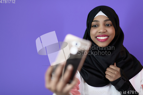 Image of african muslim woman with a beautiful smile takes a selfie with a cell phone