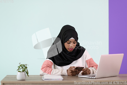 Image of afro girl wearing a hijab thoughtfully sits in her home office and uses a laptop