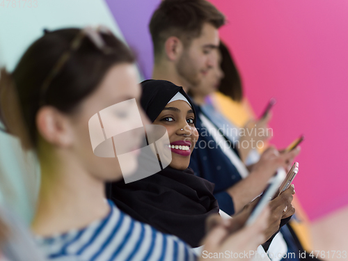 Image of diverse teenagers use mobile devices while posing for a studio photo in front of a pink background