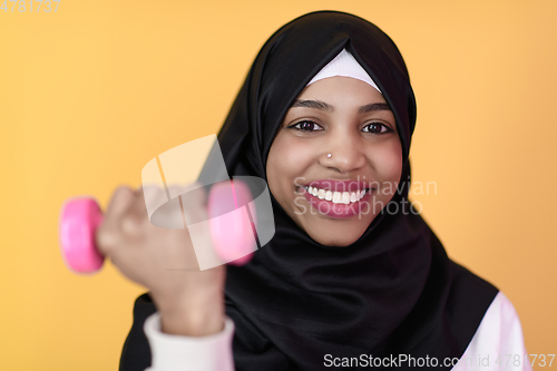 Image of afro muslim woman promotes a healthy life, holding dumbbells in her hands