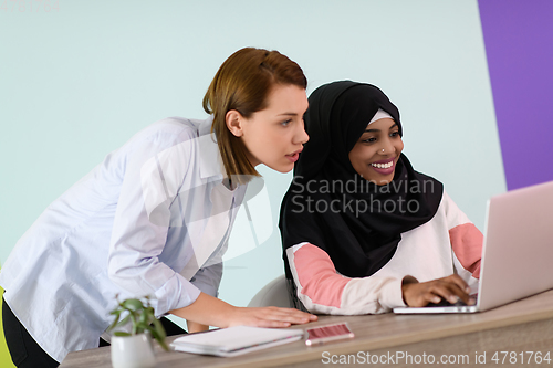 Image of afro muslim woman wearing a hijab sits smiling in her home office and using laptop for online meeting