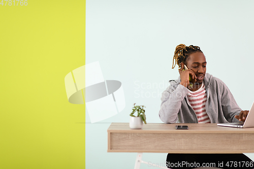 Image of afro young man sits in his home office during a pandemic and uses the phone