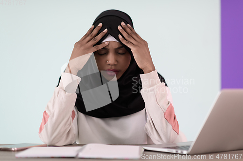 Image of afro girl wearing a hijab is disappointed and sad sitting in her home office and using a laptop