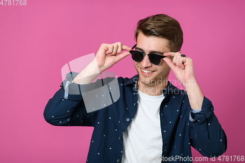 Image of a portrait of a young man wearing a blue shirt and posing in front of a pink background 