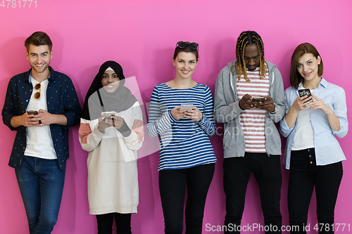 Image of diverse teenagers use mobile devices while posing for a studio photo in front of a pink background