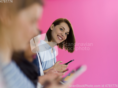 Image of diverse teenagers use mobile devices while posing for a studio photo in front of a pink background