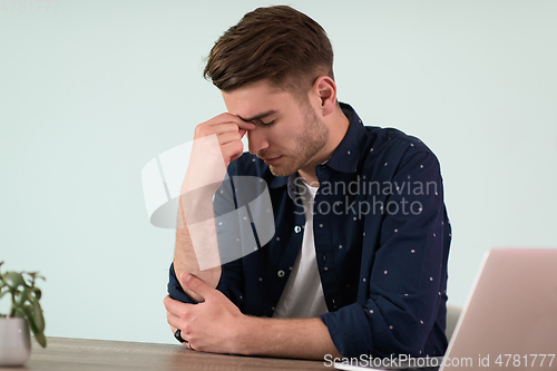 Image of disappointed and annoyed man sitting at a table and looking at a laptop