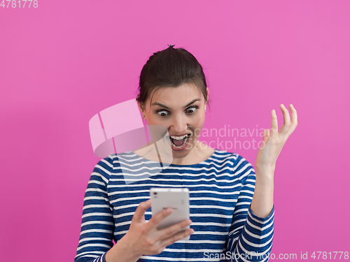 Image of surprised-faced girl looks at her cell phone as she stands in front of a pink background