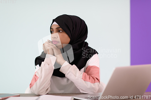 Image of afro girl wearing a hijab thoughtfully sits in her home office and uses a laptop