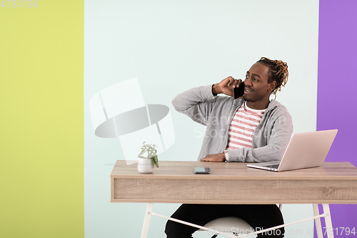 Image of afro young man sits in his home office during a pandemic and uses the phone